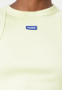 Ljusgrön ribbad tanktopp med rund halsringning och en blå broderad "HUGO"-logotyp på bröstet. Mjuk textur, figurnära design.