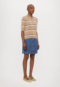 Polo shirt à rayures beiges à manches courtes avec col, associé à une jupe en denim bleu avec des rayures blanches verticales et des ballerines tissées beiges.