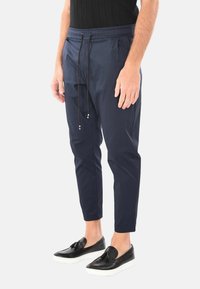 Pantaloni tapered blu navy in tessuto leggero con vita elastica e coulisse nera. Abbinati a scarpe slip-on nere.