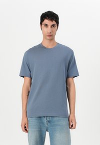 Herre t-skjorte med korte ermer i myk blå stoff, rund hals, avslappet passform, ensfarget design uten mønstre eller detaljer. Bærende med lyseblå jeans.