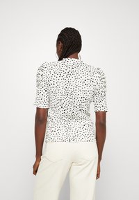 Top a maniche corte bianco con motivo a macchie nere, dotato di spalle a palloncino e design fitted.