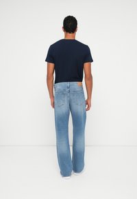 Ανοιχτό μπλε τζιν παντελόνι με άνετη εφαρμογή και φαρδιά πόδια. Η ζώνη διαθέτει ένα καφέ δερμάτινο λογότυπο. Συνδυασμένο με ένα σκούρο μπλουζάκι.