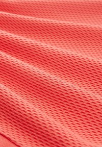 Korálový texturovaný materiál s diamantovým vzorem, který vykazuje měkký, hladký povrch a jemný lesk. Materiál se zdá být elastický a lehký.