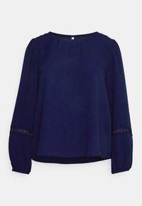 Blusa a maniche lunghe blu navy con scollo rotondo, maniche arricciate e dettagli in pizzo ai polsini. Tessuto leggero con una finitura testurizzata.