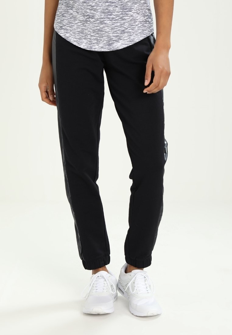 Black athletic pants with an elastic waistband, tapered legs, and side stripes, paired with white sneakers. Textured gray shirt on top.