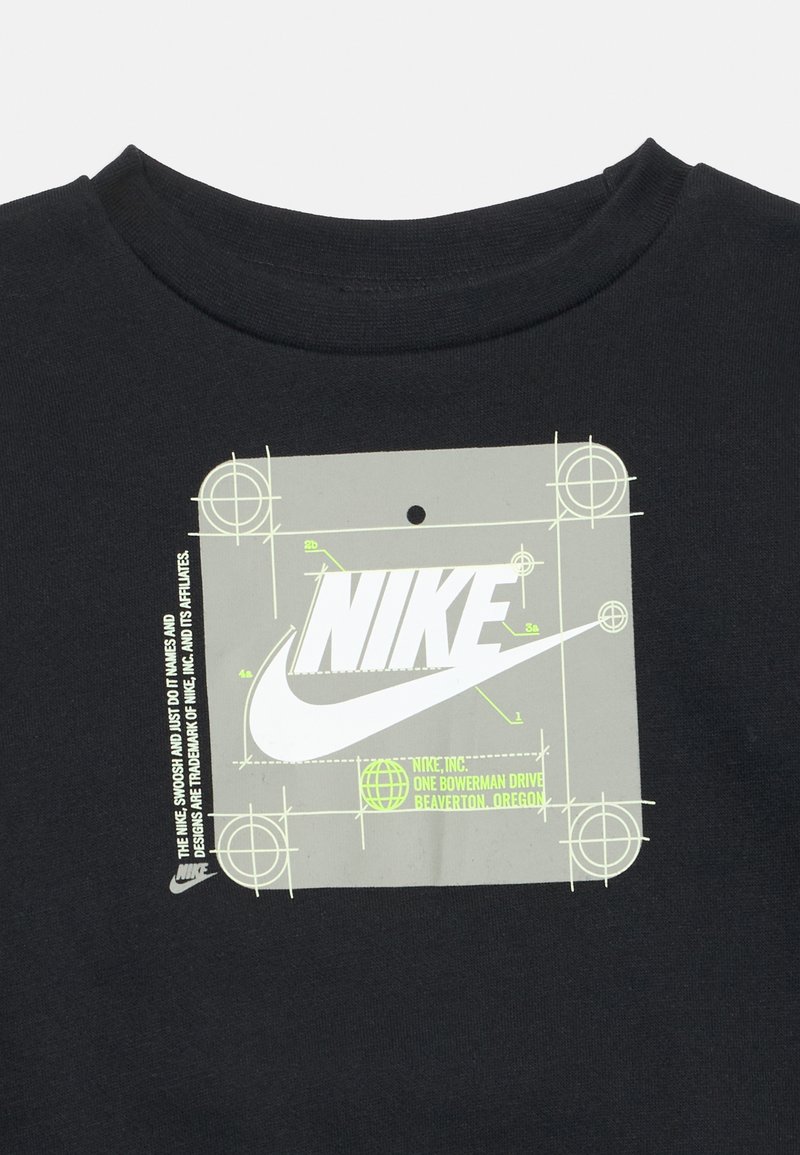 T-shirt en coton noir présentant une étiquette graphique gris clair avec le logo Nike et des éléments de design technique en accents verts.