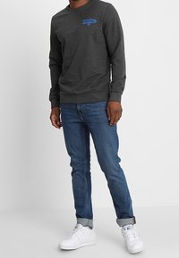 Tmavě šedá mikina s modrým logem, kulatým výstřihem, žebrovanými manžetami a lemem; doplněná modrými džíny a bílými teniskami.