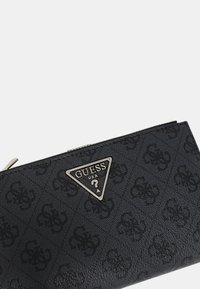 Portafoglio nero realizzato in materiale testurizzato, con un logo triangolare in argento. Sulla superficie sono presenti sottili motivi in rilievo. Chiusura con zip nella parte superiore.