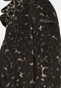 Cappotto in lana con stampa leopardata marrone scuro e nera, dotato di bottoni neri con marchio e un'etichetta "Frieda & Freddies New York" sulla manica.