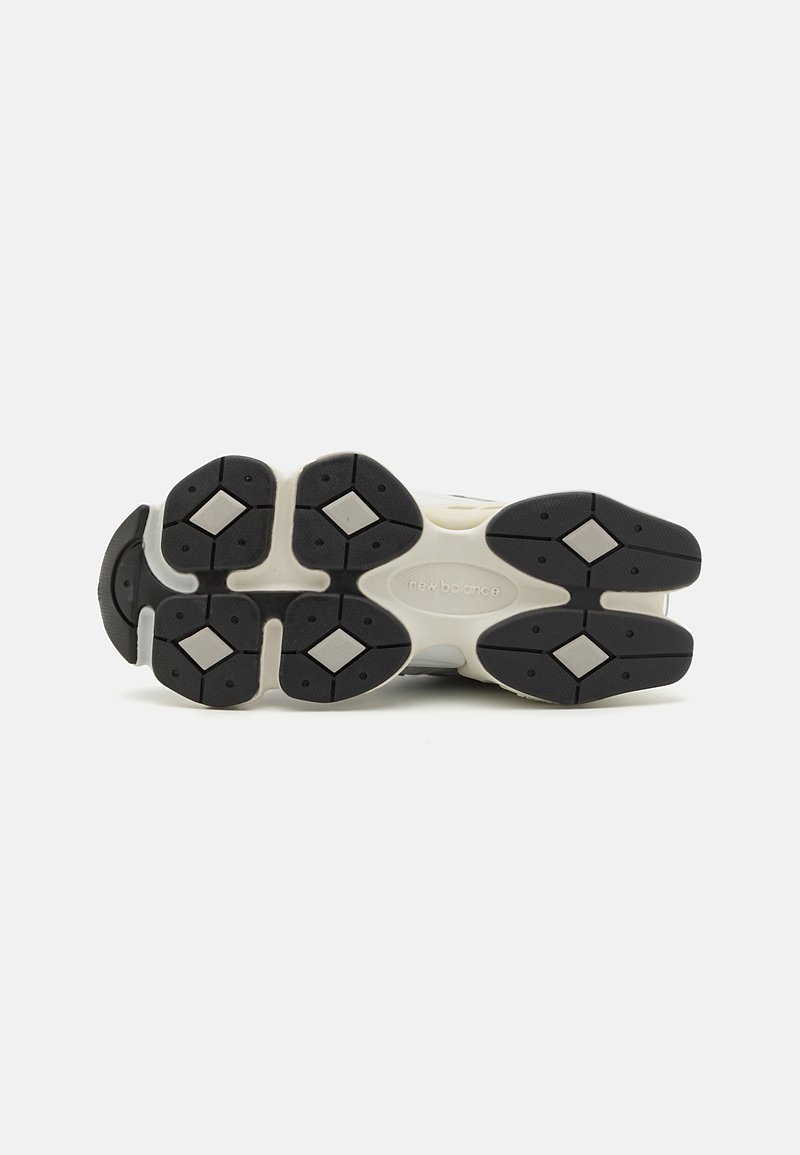 Semelle de chaussure avec une forme arrondie, arborant un dessus gris clair, une semelle extérieure en caoutchouc noir, des rainures en forme de diamant et des accents foncés.