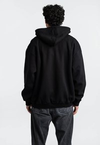 Sudadera negra con capucha y corte holgado, hecha de tela suave. Presenta puños y dobladillo de canalé, con una superficie lisa y un diseño minimalista.