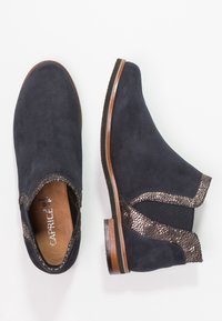 Par de botas de ante azul marino hasta el tobillo con ribete texturizado marrón y bordes de suela de madera, una mostrada desde arriba y otra desde el lado.