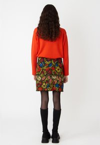 Oranje gebreide trui gecombineerd met een zwarte rok met bloemenpatroon, met levendige bloemen in rood, blauw en geel. Zwarte kniehoge laarzen.