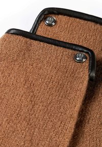 Producto de fieltro de lana marrón con ribete de cuero negro y cierres de presión metálicos, que presenta una textura suave y un diseño limpio y simple.