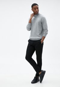 Harmaa ribatusta neuleesta, jossa on keinoturkkikaulus, yhdistetty mustiin slim-fit-housuihin ja mustiin nauhakengiin, joissa on sileä nahkapinta.