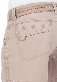 Beige Shorts aus Baumwolle mit glatter Textur, ausgestattet mit einer Gesäßtasche, die mit drei Stern-Stickereien verziert ist, sowie einem hellbraunen Gürtel mit roten Nähten.
