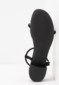 Sandales en suède noir avec de fines lanières et une semelle en caoutchouc texturé. Présente un talon lisse et des accents transparents. Taille 37 indiquée sur la semelle.