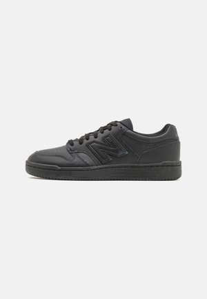 Black athletic shoes with a smooth leather upper, textured accents, and a rubber sole. Features a lace closure and a prominent logo on the side.