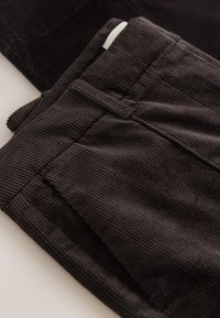 Pantaloni in velluto a coste neri con trama a coste, dotati di fronte piatto e tasche laterali. Il tessuto ha un aspetto morbido e vellutato.