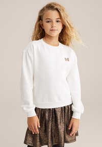 Witte sweatshirt met geribbelde mouwen, voorzien van een klein, reliëf goudkleurig vlinderontwerp en een relaxte pasvorm, gecombineerd met een glanzige bronzen rok.