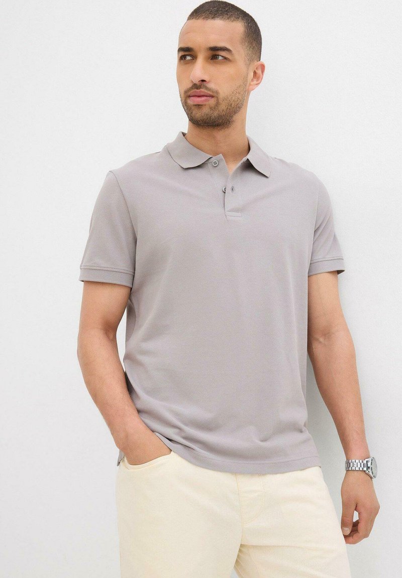 Polo grigio chiaro con una consistenza morbida, colletto pieghevole e patta con tre bottoni; abbinato a pantaloni beige. Design casual e aderente.