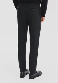 Czarne spodnie wykonane z gładkiego materiału o zwężanym kroju. Posiadają elastyczny pas i dwie tylne kieszenie, z czego jedna z guzikem.