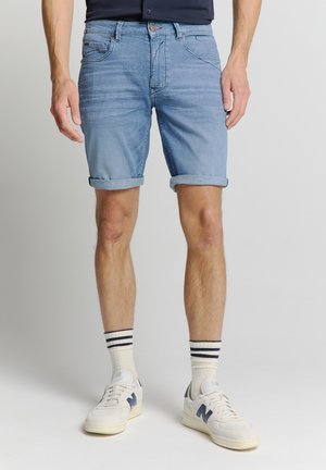 Shorts en denim bleu clair avec poignets retroussés, poches avant et fermeture à bouton. Associés à des baskets blanches et des chaussettes à rayures.