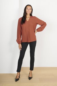 Roestbruine blouse met lange mouwen en gestructureerde stippen, V-hals, gecombineerd met zwarte slim-fit broek en zwarte puntige hakken. Eenvoudig, modern ontwerp.
