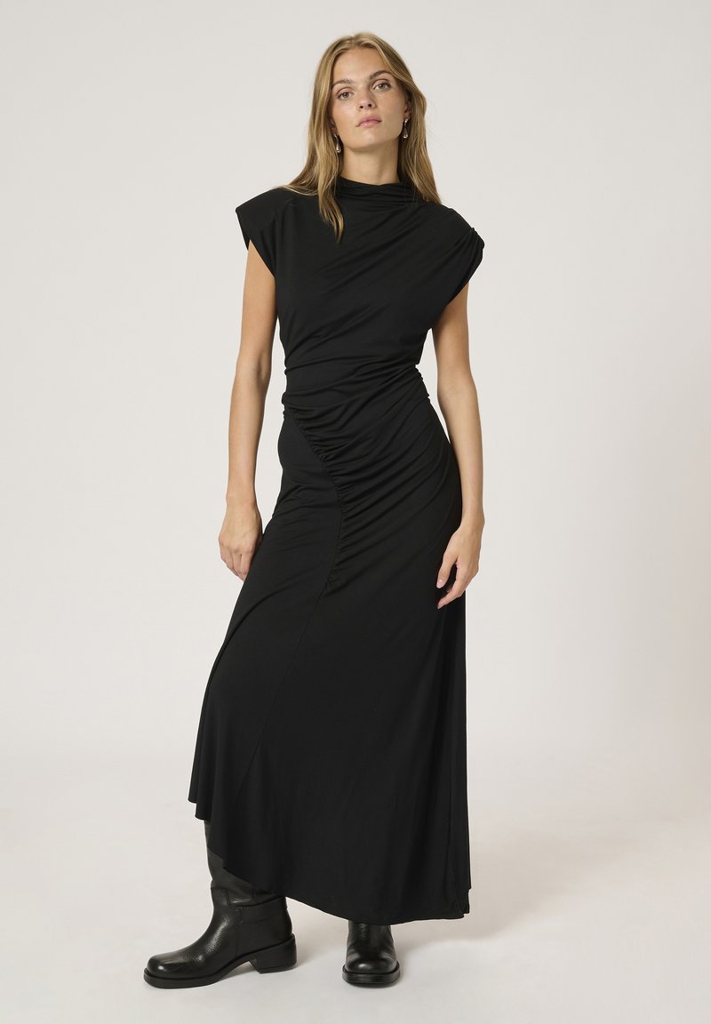 Abito maxi nero elasticizzato con maniche a cappuccio, design drappeggiato e dettagli arricciati in vita, abbinato a stivali neri alla caviglia.