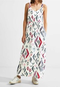 Robe longue en tissu léger avec une base blanche ornée de motifs géométriques multicolores. Associée à des baskets beiges.