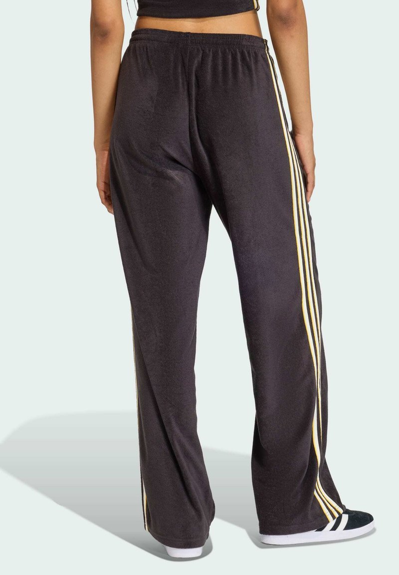 Pantaloni della tuta neri con strisce gialle sui lati, caratterizzati da una vestibilità ampia e una vita elastica. Il tessuto appare morbido e strutturato.