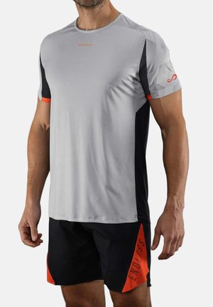 Man die een grijs-zwart sportshirt met korte mouwen en zwarte shorts met oranje driehoekige accenten en de tekst "ENDLESS" draagt.