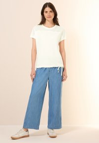 T-shirt vert clair à manches courtes avec un haut en mesh et un ourlet à cordon, associé à un pantalon en denim bleu clair à jambes larges et des baskets blanches.