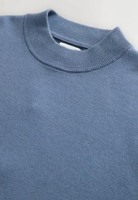 Niebieski sweter z dzianiny z ribbowanym okrągłym dekoltem, miękką teksturą i bezszwowym wykończeniem. Tkanina wydaje się gładka z subtelnymi odcieniami kolorów.