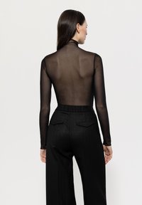 Schwarzes, durchscheinendes Langarmoberteil mit hohem Ausschnitt, kombiniert mit schwarzen, gestreiften weit geschnittenen Hosen mit Taschen.