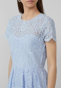 Hellblaues Kleid mit floraler Spitze, transparentem Oberteil, kurzen Ärmeln, gesäumten Kanten und einem ausgestellten Rock. Strukturierte Spitzenmit details.