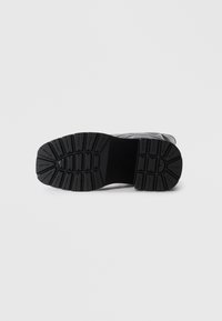 Black rubber shoe sole featuring a patterned tread for grip and stability, with a smooth upper portion transitioning to the sole.