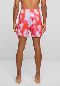 Červené a ružové plážové šortky s farbením tie-dye, s elastickým pásom, vo voľnom strihu a hladkej textúre, nosené s svetlými šľapkami.