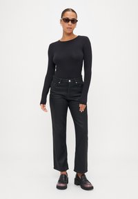 Top negro de manga larga, jeans negros de cintura alta y mocasines negros con plataforma. Los accesorios incluyen gafas de sol negras delgadas y pequeños pendientes de aro.