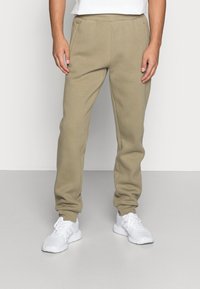 Beige joggerbyxor med en avsmalnande passform, tillverkade av mjukt bomullsblandat tyg; har elastisk midja och mudd, sidofickor och minimala sömmar.