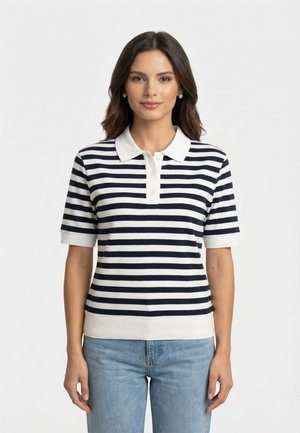 Donna con polo a maniche corte a righe orizzontali nere e bianche e jeans azzurri, in piedi davanti a uno sfondo bianco uniforme.