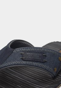 Κοντινό πλάνο ενός σανδαλιού Skechers σε ναυτικό μπλε χρώμα με υφασμάτινο λουράκι, υφή στο πέλμα και ετικέτα που γράφει "Skechers est. 1992 California."