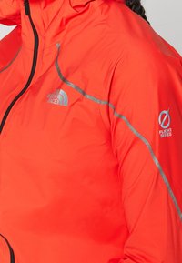 Nahaufnahme einer leuchtend roten North Face Flight Series Jacke mit reflektierenden grauen Streifen an Schulter und Ärmel.