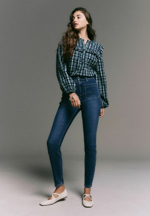 Kostkovaná košile s volánkovými detaily, džíny s vysokým pasem a bílé ploché boty. Tmavě modrá barva s hladkým texturem a přiléhavým střihem.