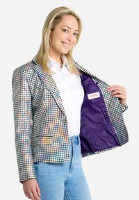 Iridescent suknja z mrežno vzorcem, sprednjima žepoma in vijoličastim satenskim podloženjem. V kombinaciji z belo srajco in modrimi kavbojkami.