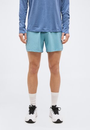 Personne portant un short de sport bleu clair, un haut à manches longues bleu, des chaussettes blanches et des chaussures de course blanches avec des lacets noirs.