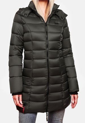 Femme portant un long manteau matelassé noir avec fermeture éclair frontale, col haut et poches latérales, assorti à un jean gris clair.