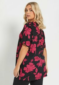 Top negro con grandes patrones florales rojos, mangas cortas, corte relajado, tejido texturizado y aberturas laterales para facilitar el movimiento.