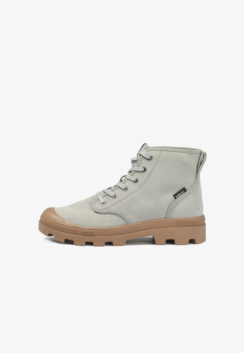 Botte montante en toile gris clair avec semelle en caoutchouc marron et bout renforcé, fermeture à lacets à l'avant, et étiquette de marque Aigle sur le côté.