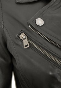 Schwarze Lederjacke mit silbernem Reißverschluss und Druckknopfdetails, sichtbaren Nähten und glatter Textur.